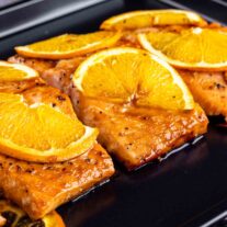 Orange Glazed Salmon topped with orange slices on a cooking pan.