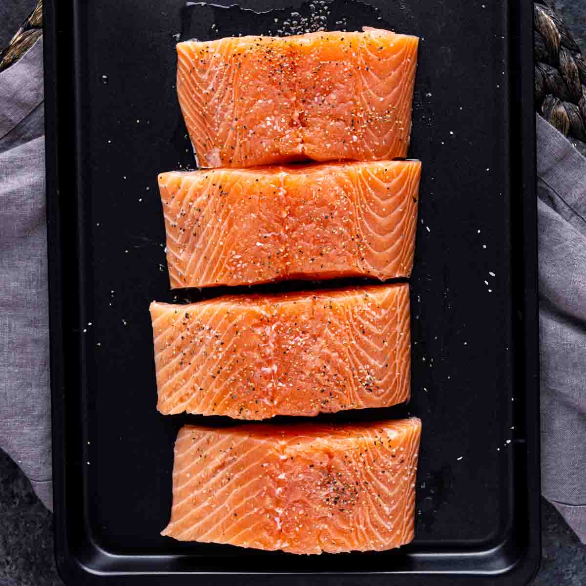 Four raw seasoned Orange Glazed Salmon on a baking sheet.