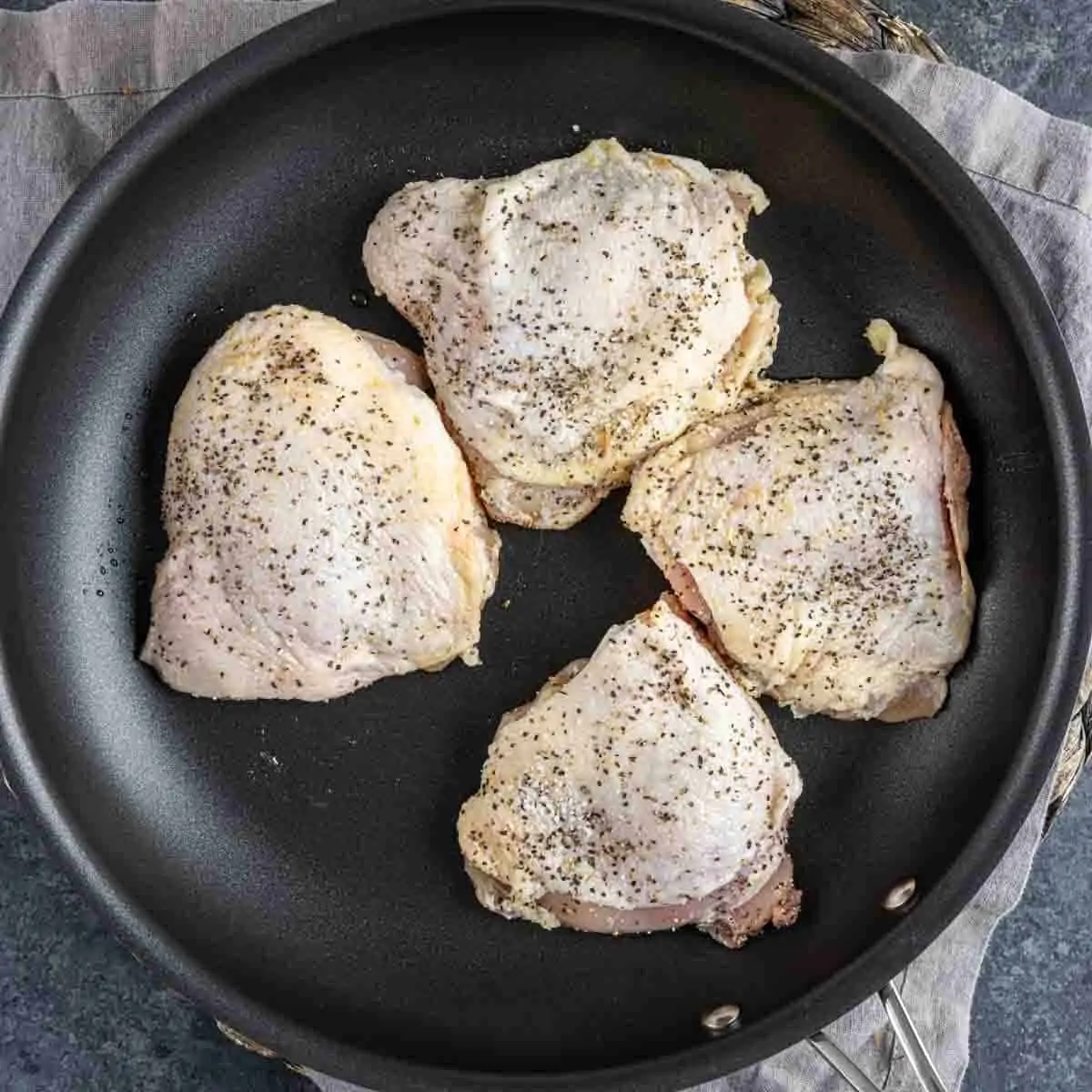 Four seasoned chicken thighs being cooked in a non-stick frying pan for Parmesan Chicken Orzo