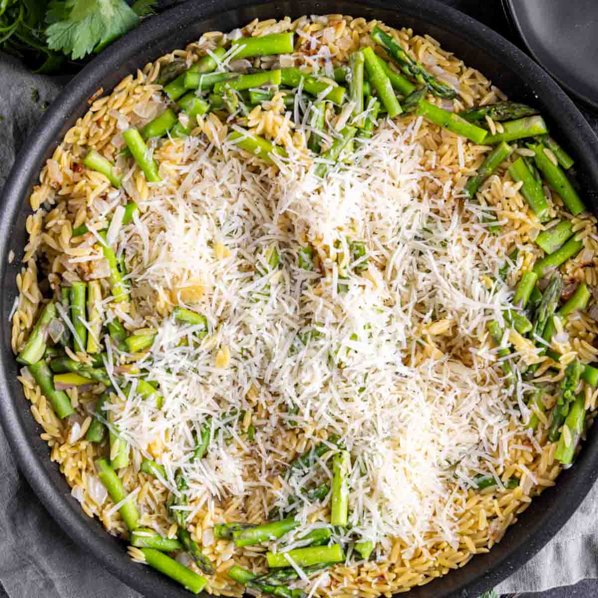 A skillet of Parmesan Chicken Orzo with asparagus and grated cheese on top.