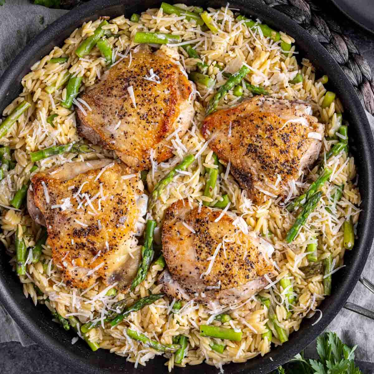 Parmesan Chicken Orzo served over a bed of rice and asparagus, garnished with grated cheese.