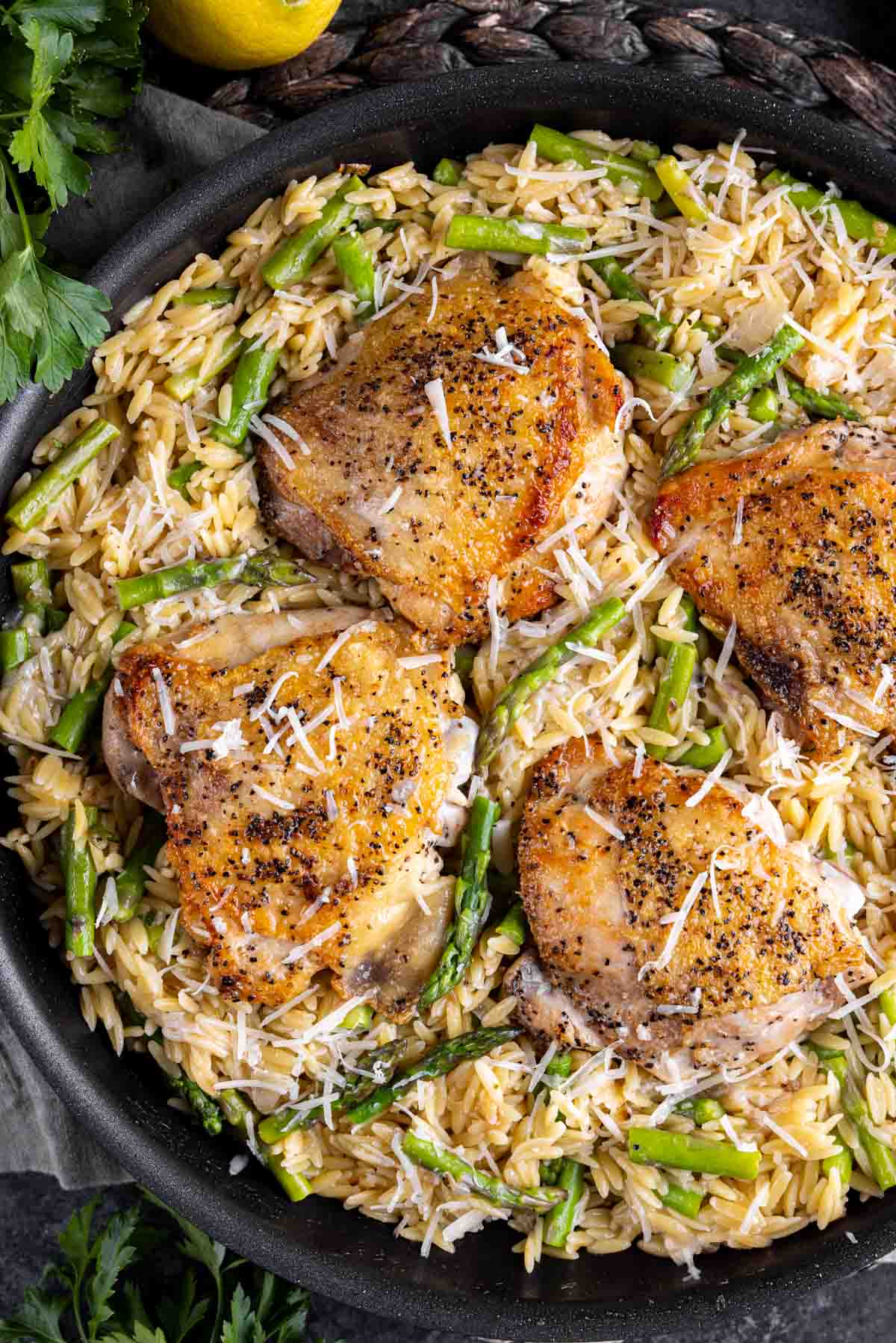 Four Parmesan Chicken Orzo served over a bed of rice and asparagus in a black skillet.