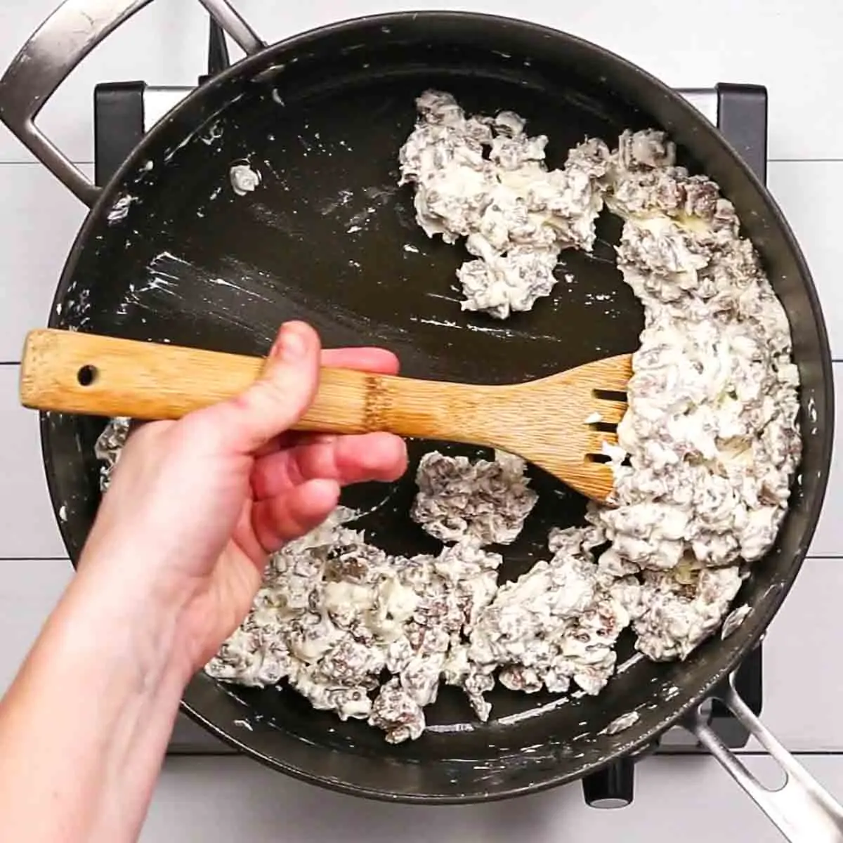 Stirring a creamy sausage mixture in a black frying pan with a wooden spatula to make Spinach and Sausage Quiche