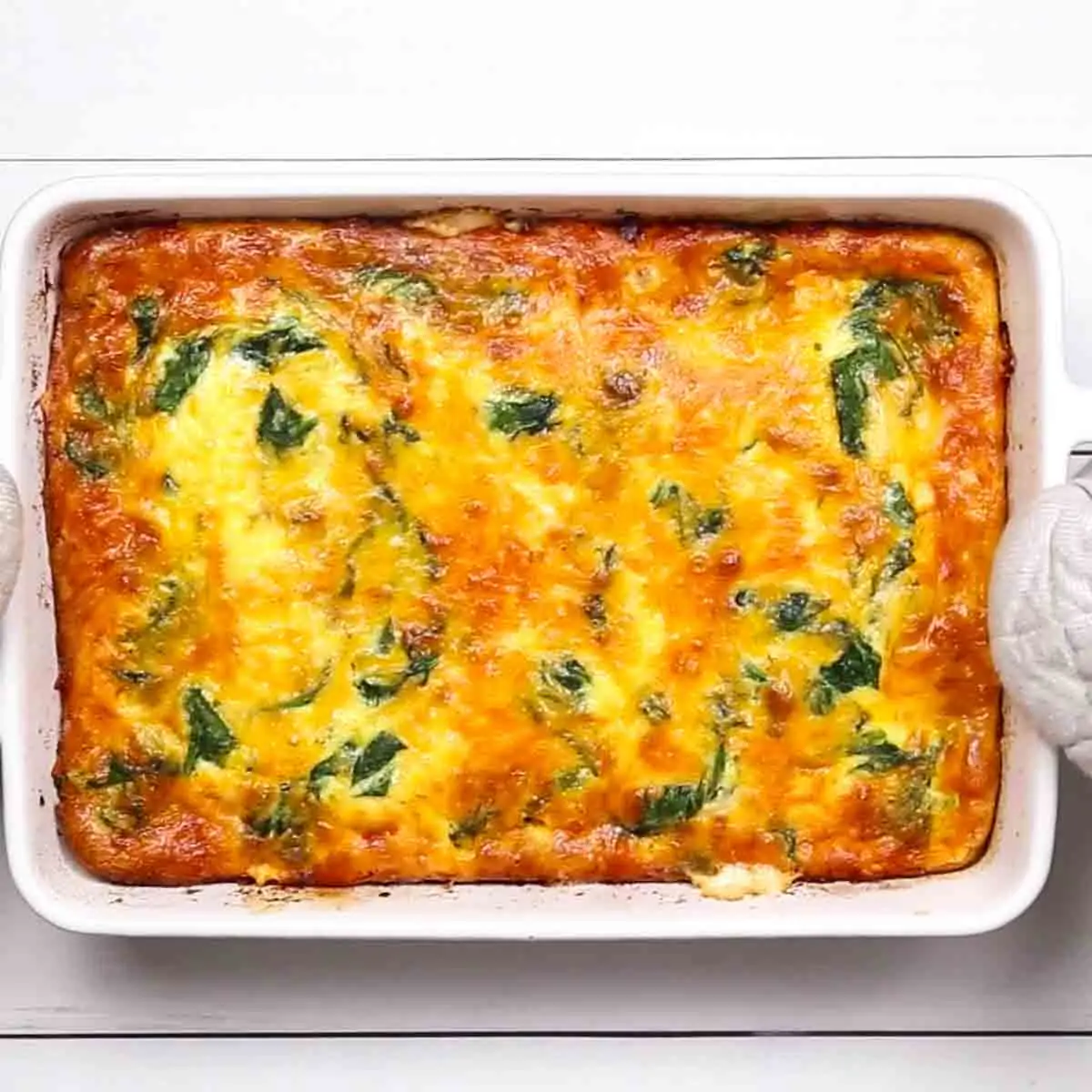 Baked Spinach and Sausage Quiche with melted cheese and spinach in a white dish.