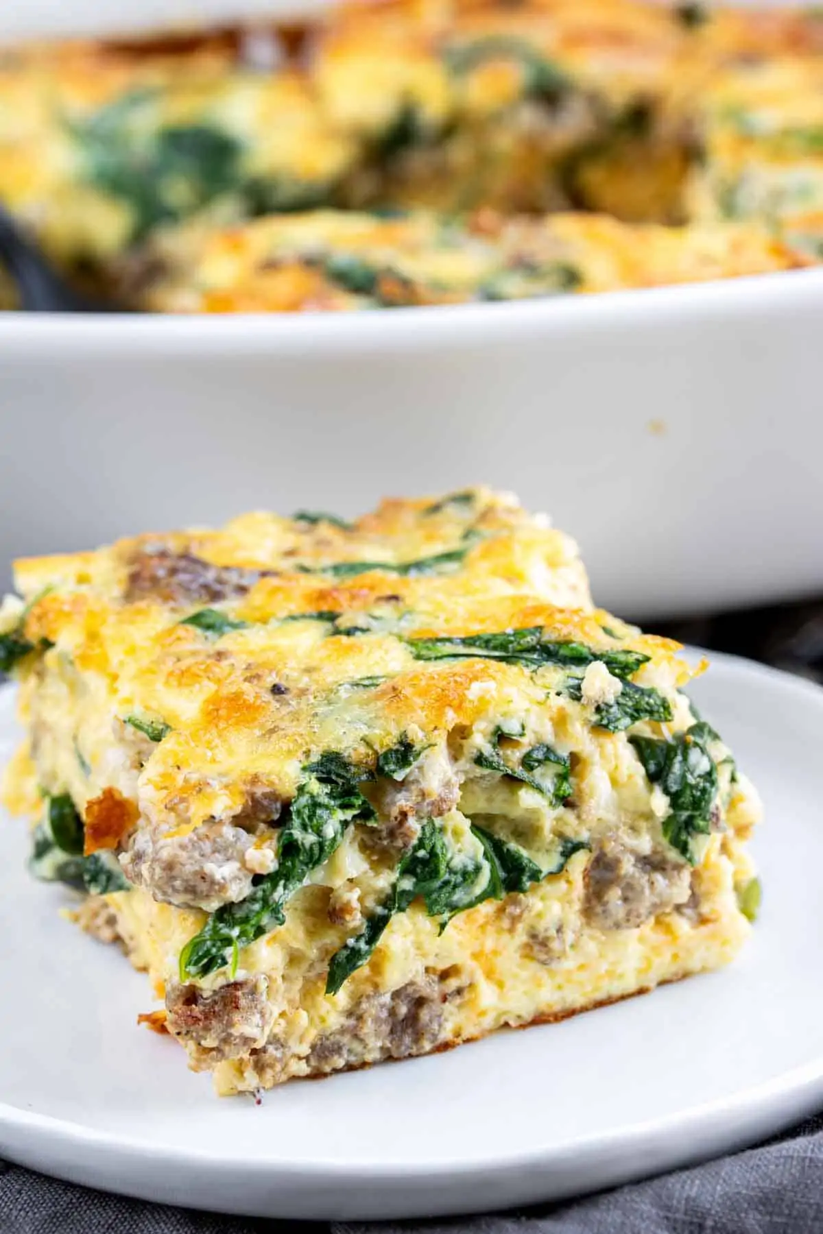 A slice of a Spinach and Sausage Quiche on a white plate.