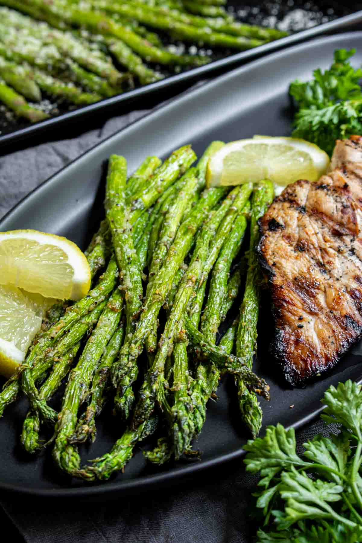 Grilled chicken breast with lemon and a side of Air Fryer Asparagus on a black plate.