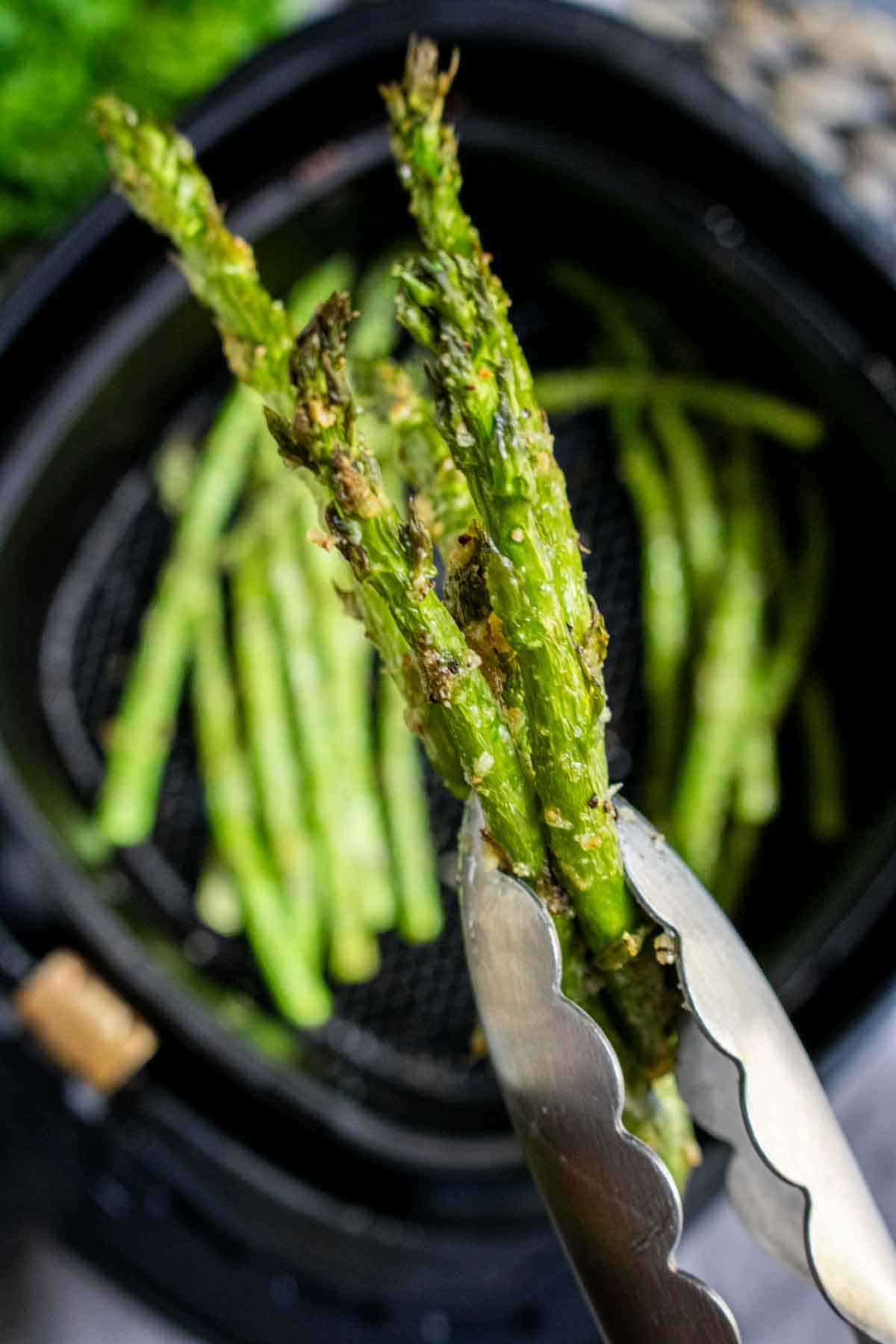 Air Fryer Asparagus being served with tongs from an air fryer.