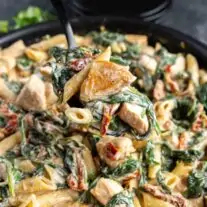 A fork lifting a creamy Chicken Florentine Casserole from a black bowl.