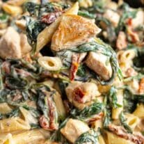A close-up of creamy penne pasta with spinach and chicken in a skillet.
