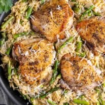 Chicken thighs served over a bed of rice and asparagus in a skillet.