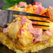 A close-up of a cheesy scrambled egg dish with ham on a fork.