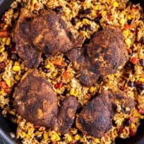 Spicy chicken thighs served on a bed of rice mixed with beans and vegetables in a skillet.