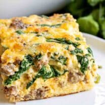 A slice of spinach and sausage breakfast casserole on a white plate.