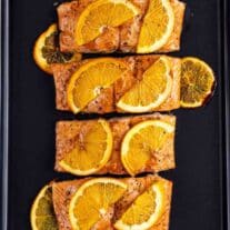 Slices of grilled salmon topped with orange slices on a black surface.
