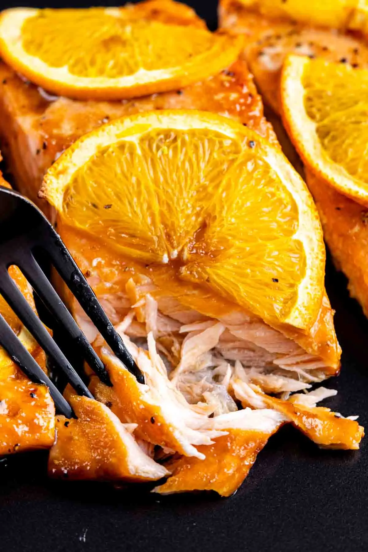Orange Glazed Salmon fillets served with slices of orange on a black plate.