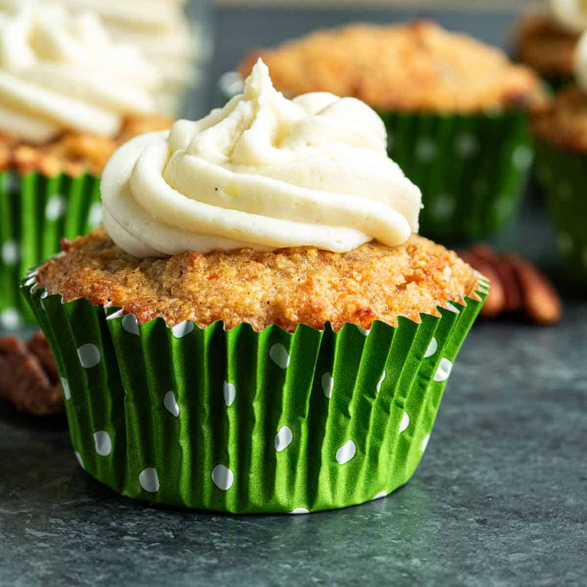 A freshly baked Keto Carrot Cake with cream cheese frosting in a green cupcake liner.