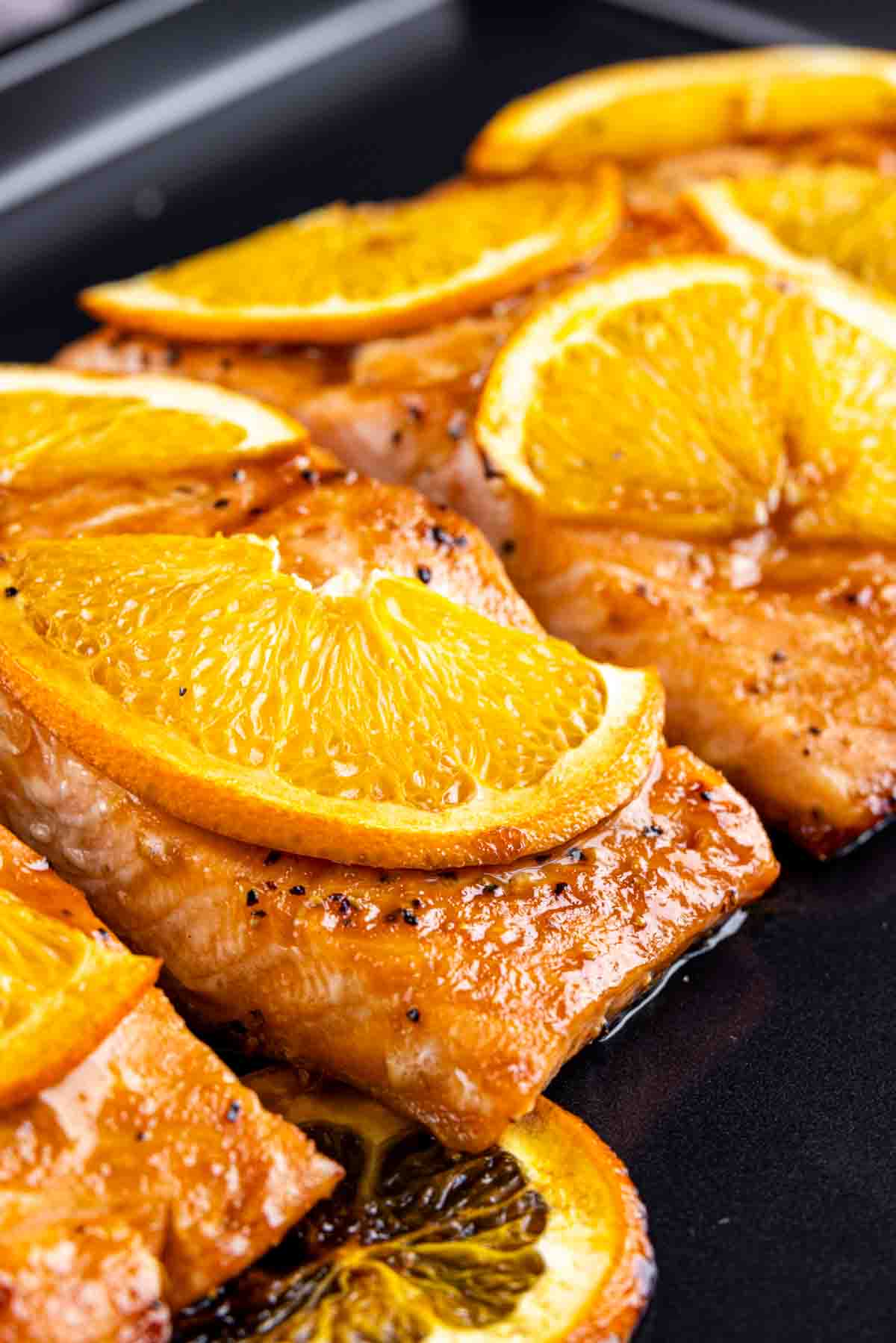 Orange Glazed Salmon topped with orange slices on a cooking surface.