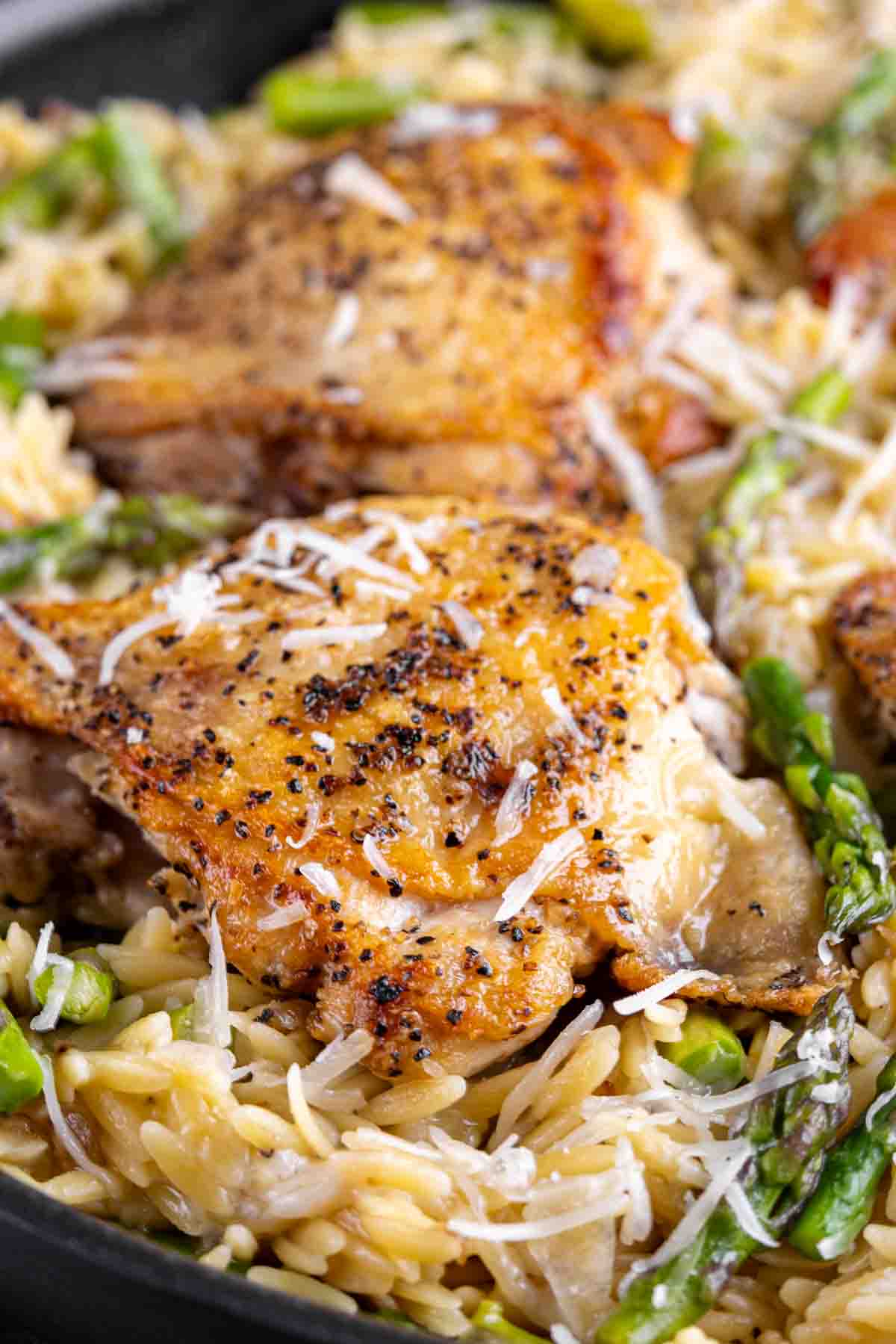 Parmesan Chicken Orzo served over a bed of orzo pasta with asparagus and topped with grated cheese.