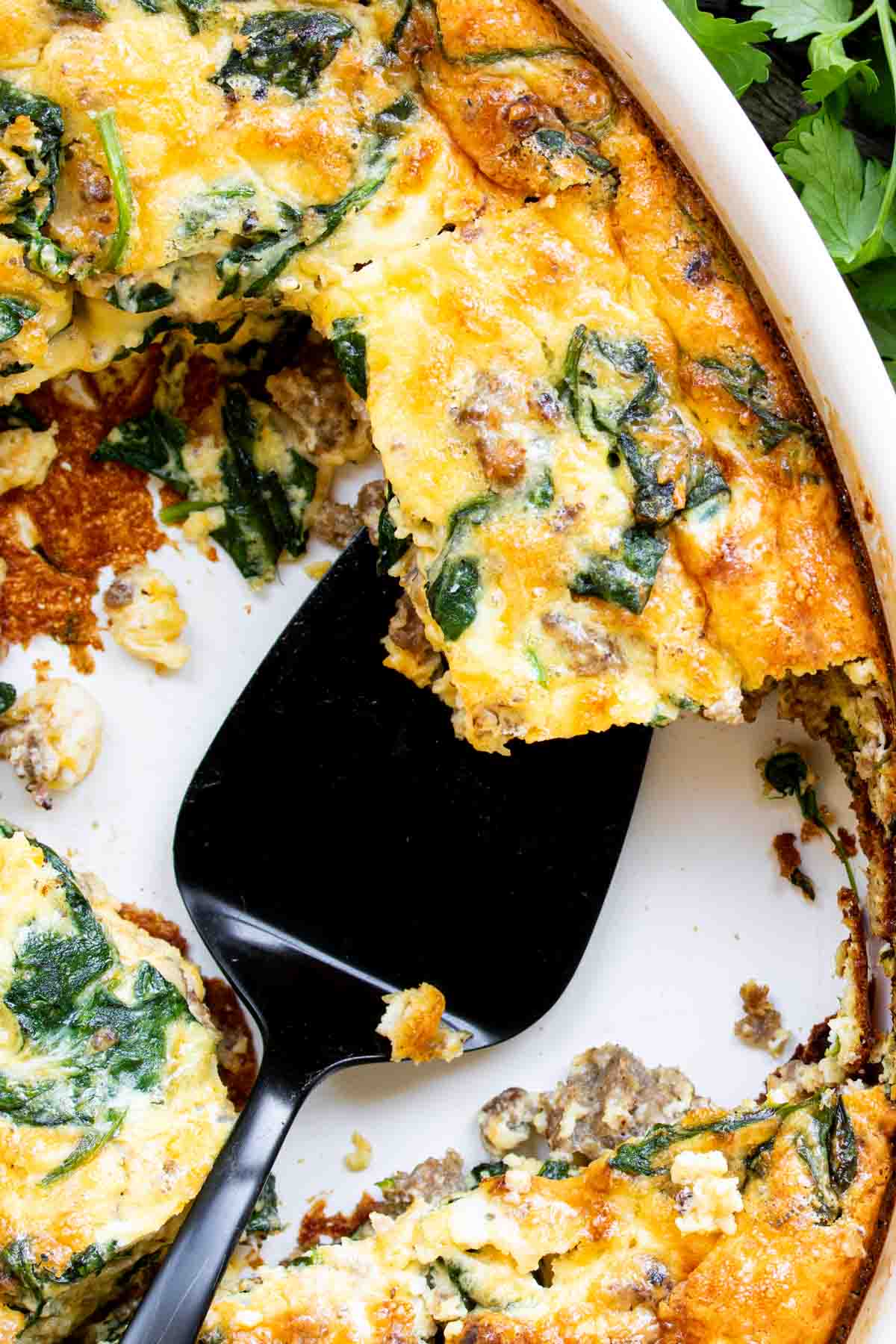 A freshly baked Spinach and Sausage Quiche with a slice being served.