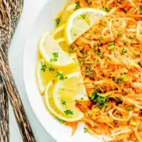 A plate of grated carrot salad garnished with lemon slices and parsley.