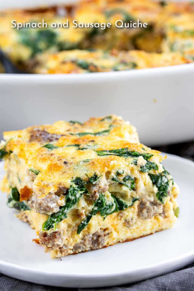 A slice of spinach and sausage quiche on a white plate with the quiche dish in the background.