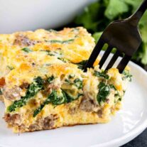 A slice of Spinach and Sausage Quiche on a plate with a fork.