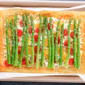 Freshly baked Asparagus Goat Cheese Tart with cherry tomatoes and cheese on a parchment-lined baking tray.