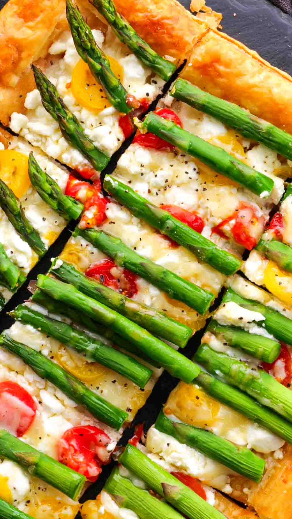 An appetizing Asparagus Goat Cheese Tart with asparagus, cheese, and tomatoes served in slices.