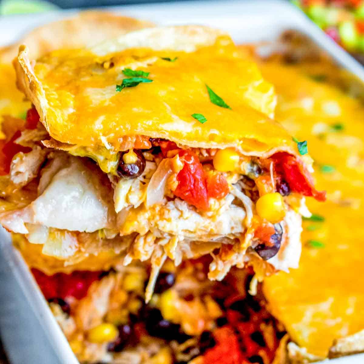 A close-up of a Chicken Tortilla Casserole slice topped with melted cheese, showing layers with vegetables and beans.