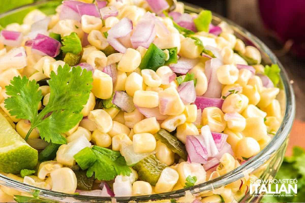 A vibrant bowl of corn salad garnished with red onion, cilantro, and lime slices, showcasing fresh and colorful ingredients.