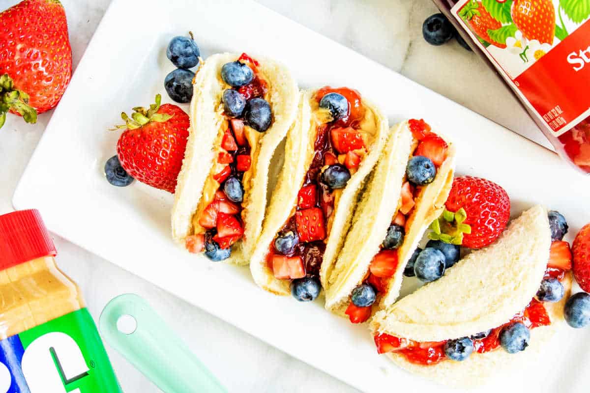 Peanut butter and jelly sandwiches cut into triangles, served with fresh strawberries and blueberries on a white plate.