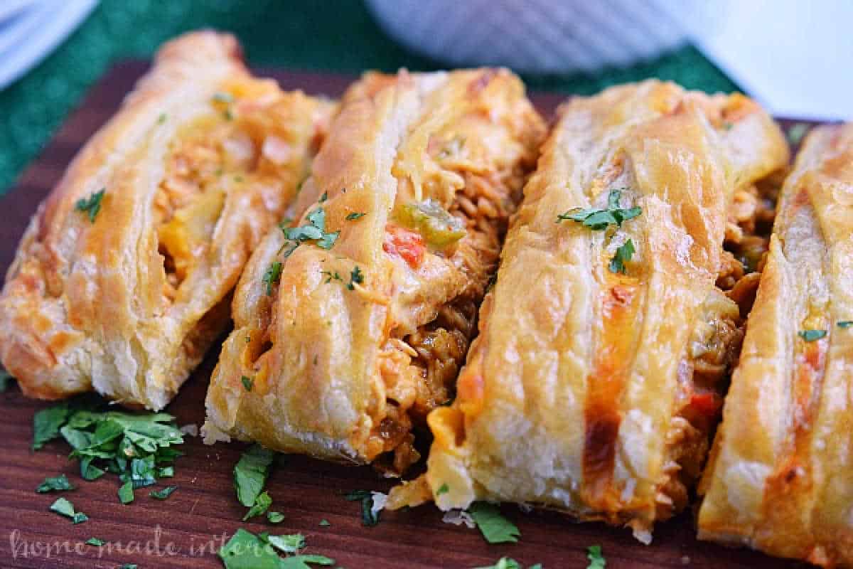 Sliced chicken pot pie with a flaky crust and visible vegetable fillings, garnished with chopped parsley on a wooden board.