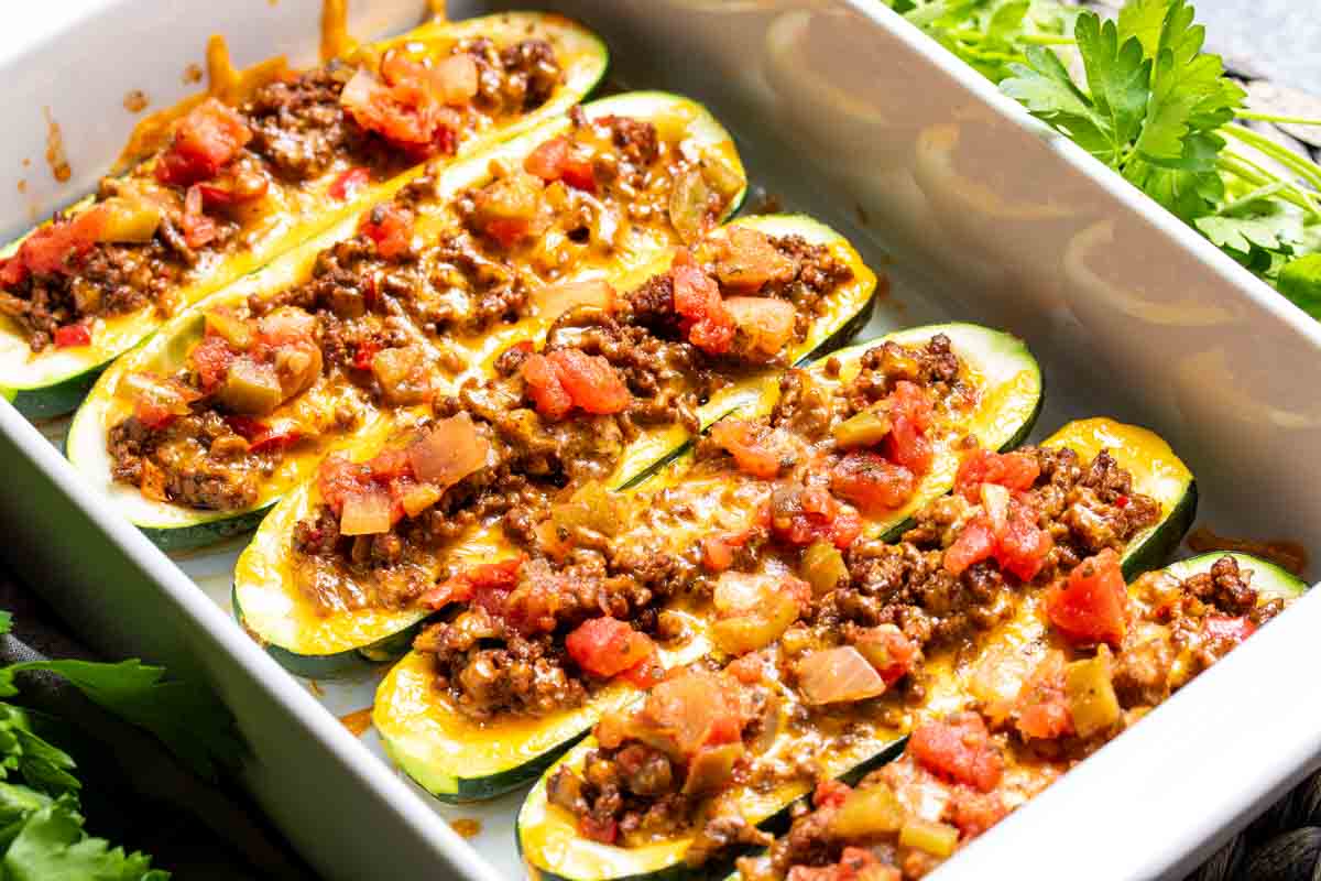 Baked zucchini boats filled with ground beef, melted cheese, and diced tomatoes, garnished with fresh parsley.