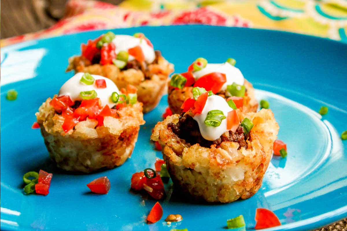 Three stuffed rice cups topped with sour cream and garnished with diced tomatoes and green onions, served on a bright blue plate.