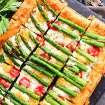 A sliced asparagus and tomato tart garnished with herbs.