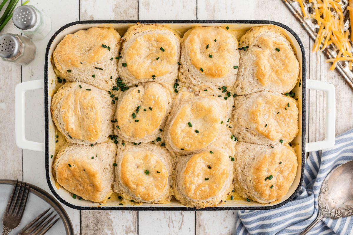 A baking dish containing sausage gravy with golden-brown biscuits, garnished with chopped herbs.