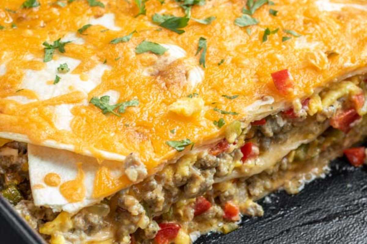 Close-up of a cheesy breakfast buttiro casserole topped with melted cheese and chopped peppers in a black dish.