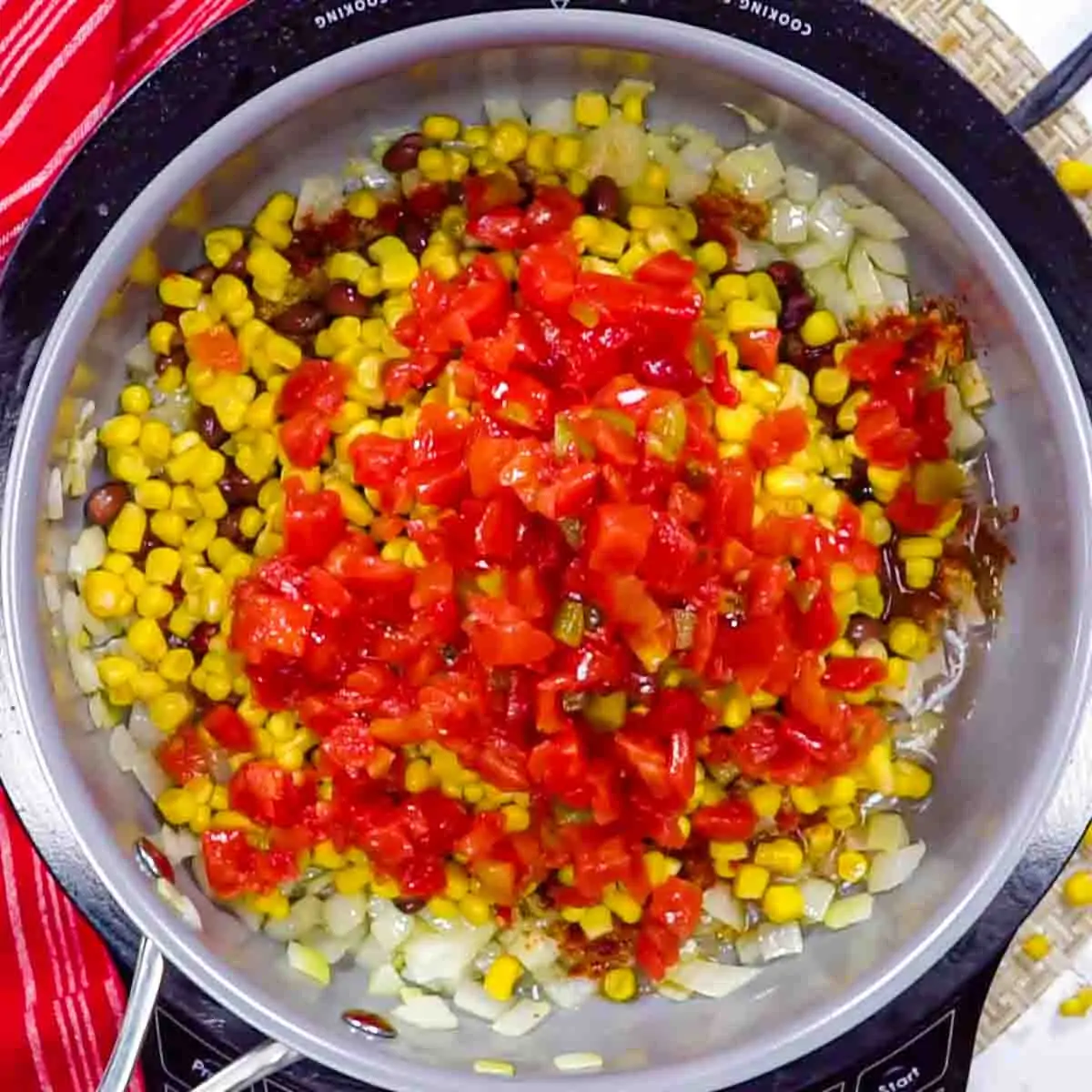 A pot containing a mix of diced onions, corn, black beans, and chopped red tomatoes, viewed from above to make filling for Chicken Tortilla Casserole
