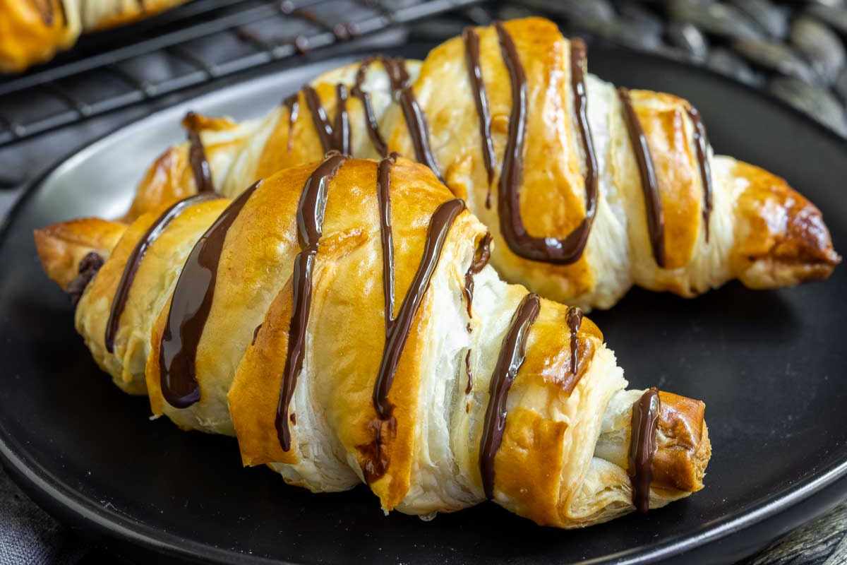 Freshly baked croissants with chocolate drizzle served on a black plate to celebrate Mother's Day.