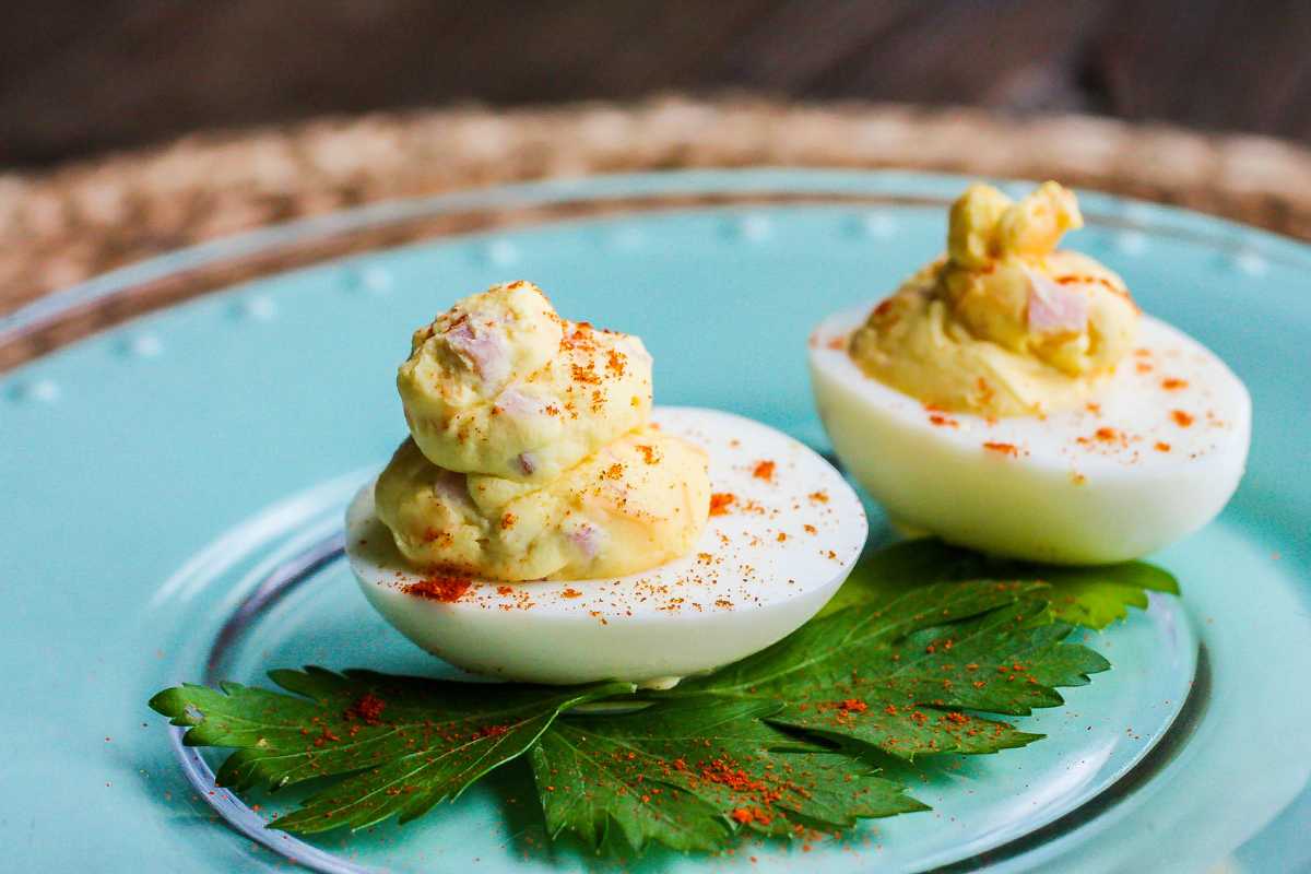 Two deviled eggs garnished with paprika on a blue plate with a green leaf, on a wooden table.