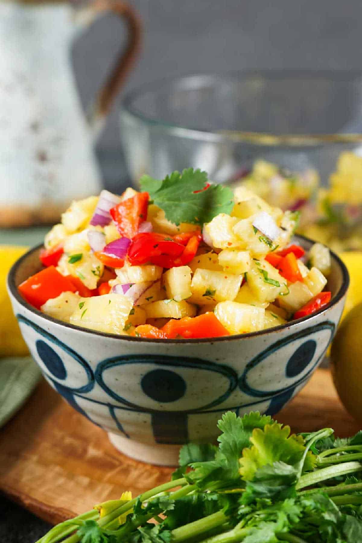A bowl of vibrant pineapple salsa with diced red onions, red bell peppers, and cilantro, presented on a wooden table.