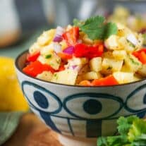 A bowl of pineapple salsa with diced red peppers, onions, and cilantro in a decorative blue and white bowl.
