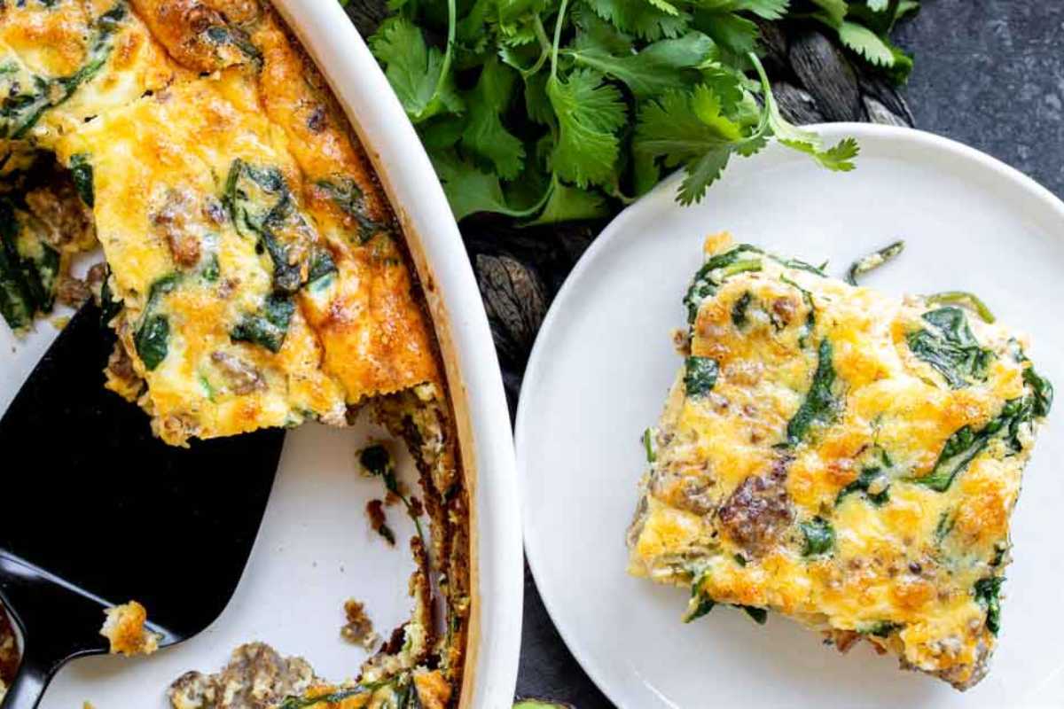 A slice of spinach and cheese frittata on a white plate with a full frittata in a ceramic dish beside it, garnished with fresh parsley.