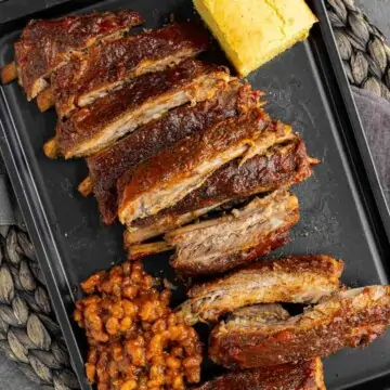 Sliced St Louis-Style Ribs on a black plate with cornbread and baked beans, viewed from above.
