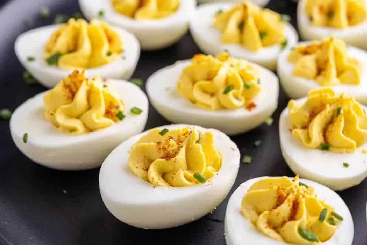 A plate of deviled eggs garnished with chopped chives and paprika.