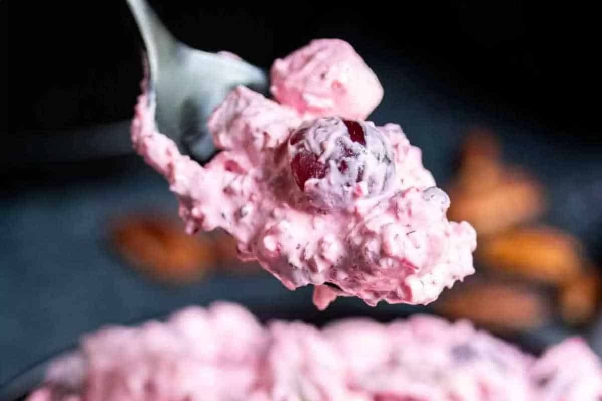 A spoonful of pink creamy dessert with grapes and whipped mixture being held above a bowl of the same dessert.