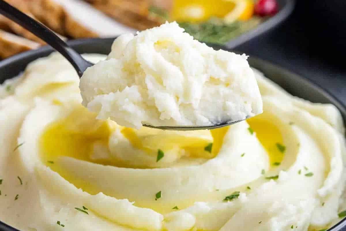 A spoonful of creamy mashed potatoes with melted butter and a sprinkle of herbs in a black bowl.