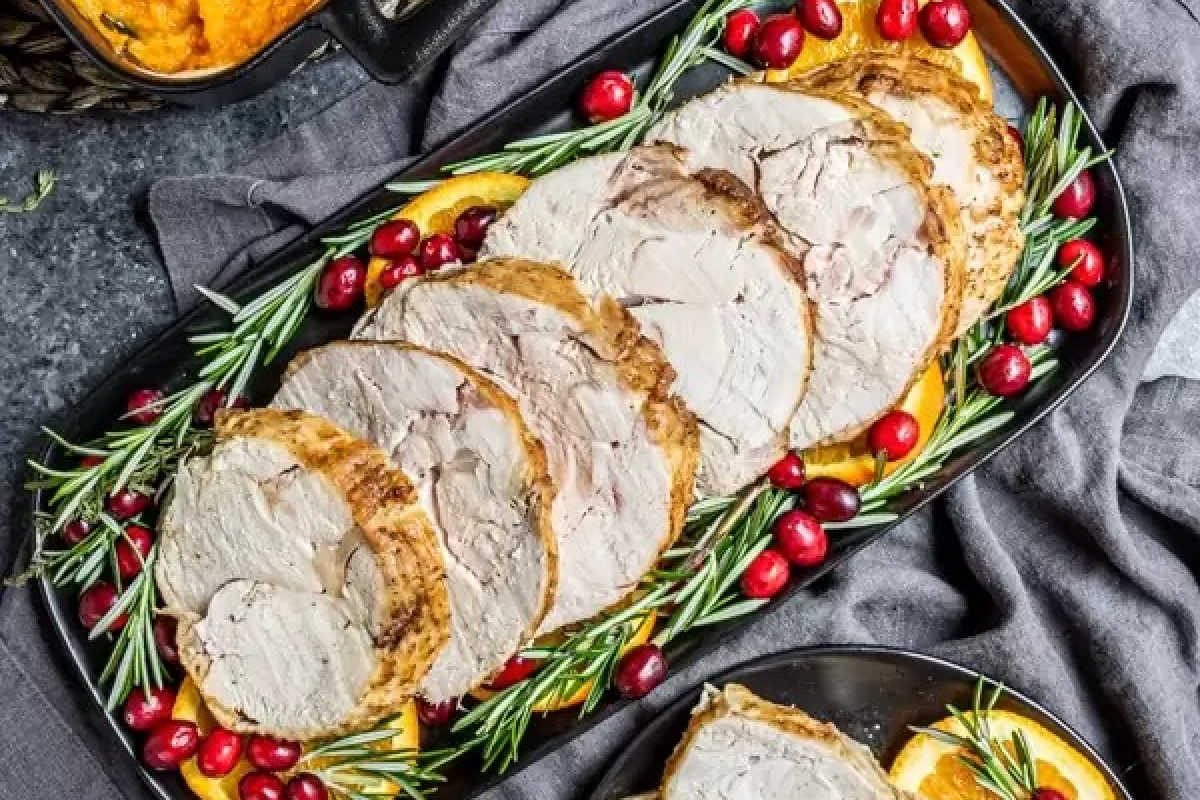 Sliced roast turkey breast arranged on a platter with fresh rosemary, cranberries, and orange slices.