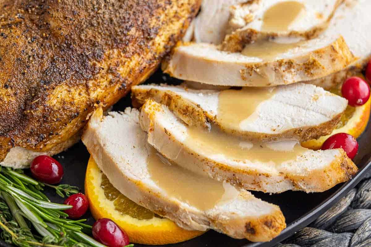 Sliced roasted turkey breast with gravy on a plate, garnished with orange slices, cranberries, and fresh rosemary.