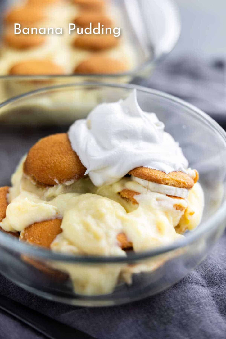 A glass bowl filled with banana pudding, vanilla wafers, and topped with a dollop of whipped cream.